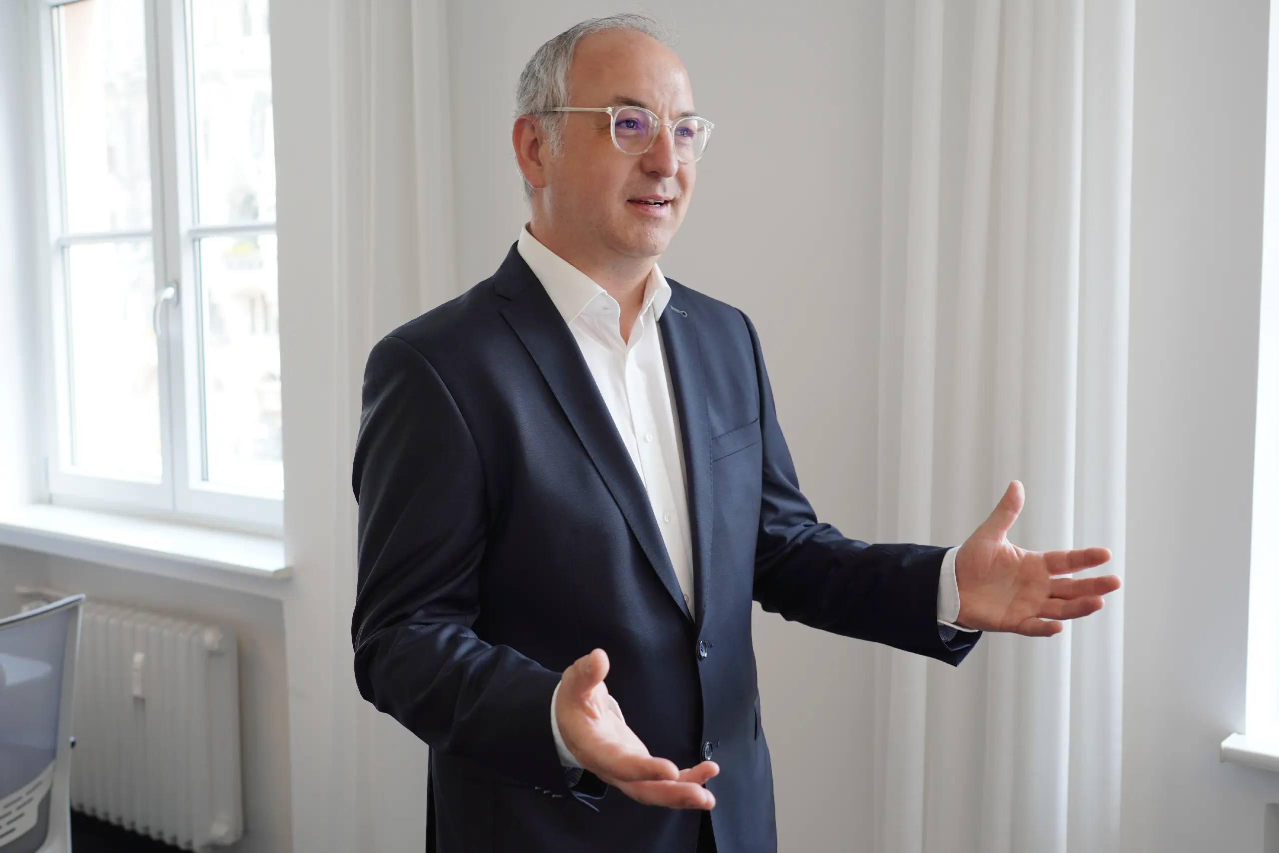 Ein Mann im Anzug gestikuliert während einer Rede im Büro der Ruess Group in München.