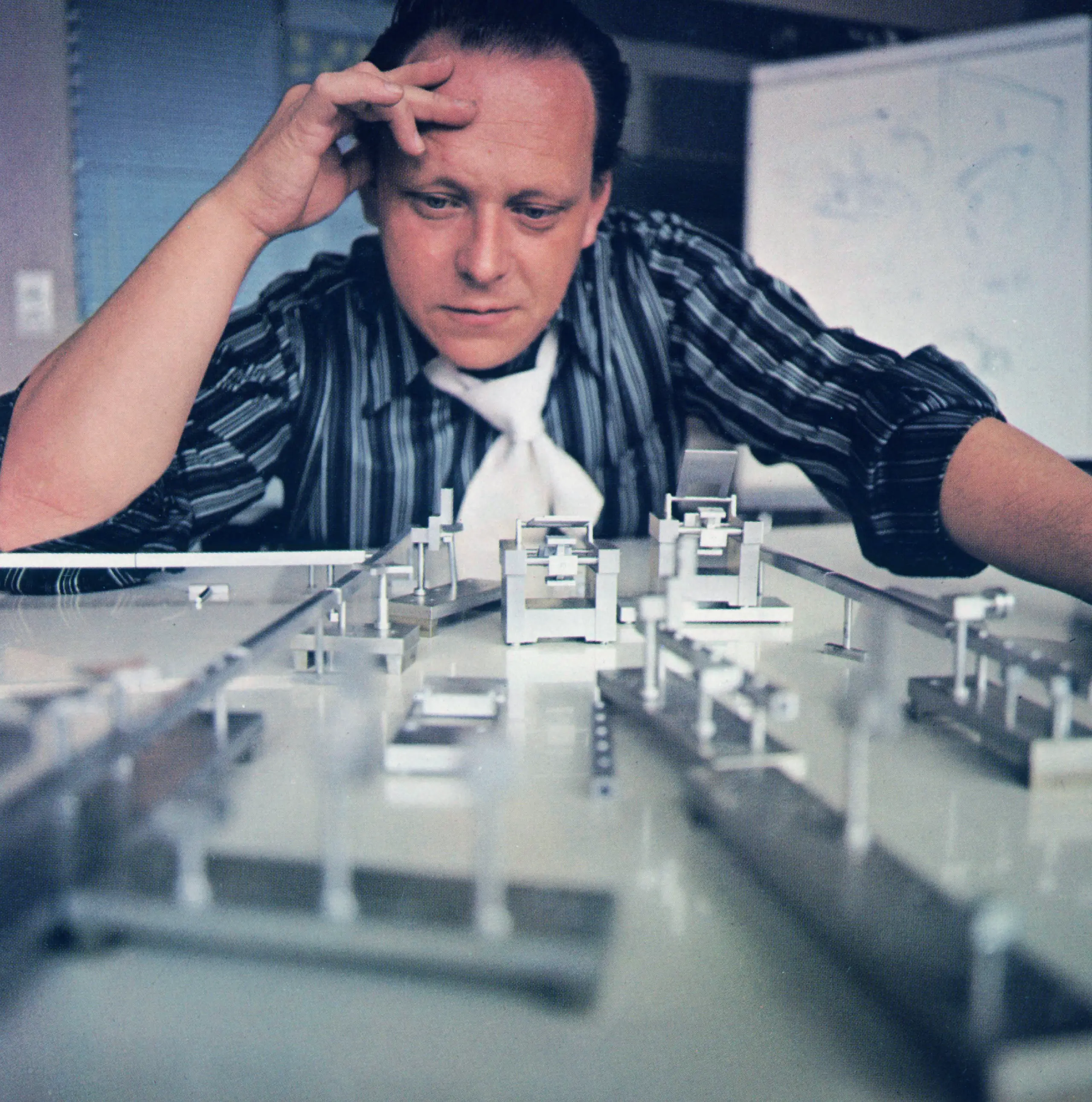 Das Bild zeigt ein Mann, der über eine Konstruktion nachdenkt, welche auf dem Tisch liegt.