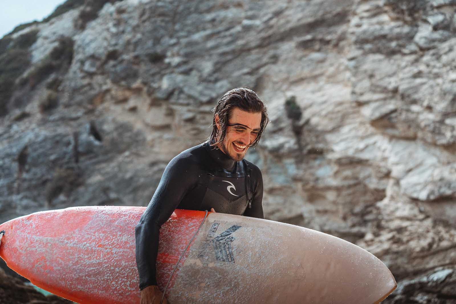 Surfer wearing a wetsuit and carrying a surfboard.