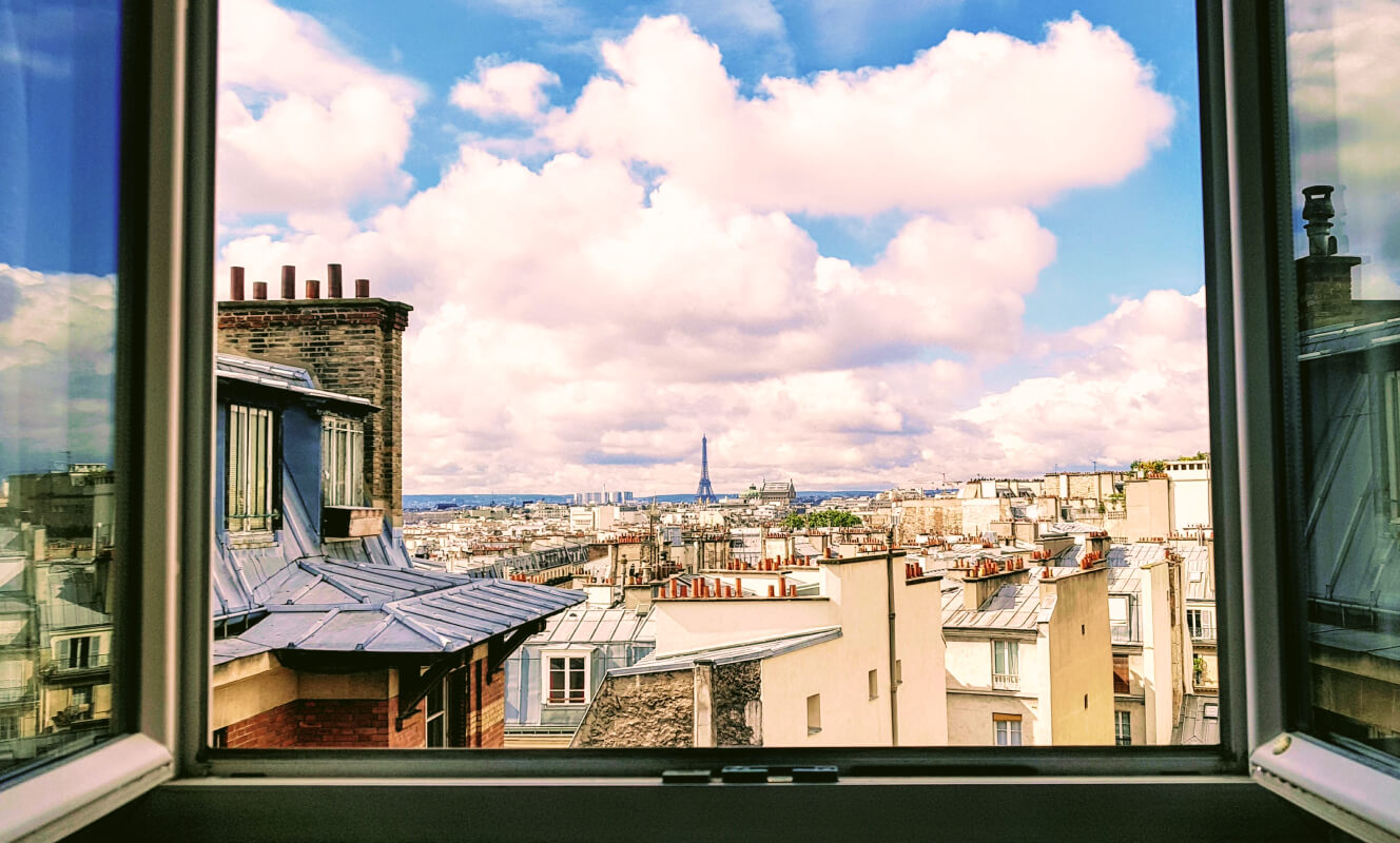 Une fenêtre parisienne est grande ouverte. Au loin, la tour Eiffel. 