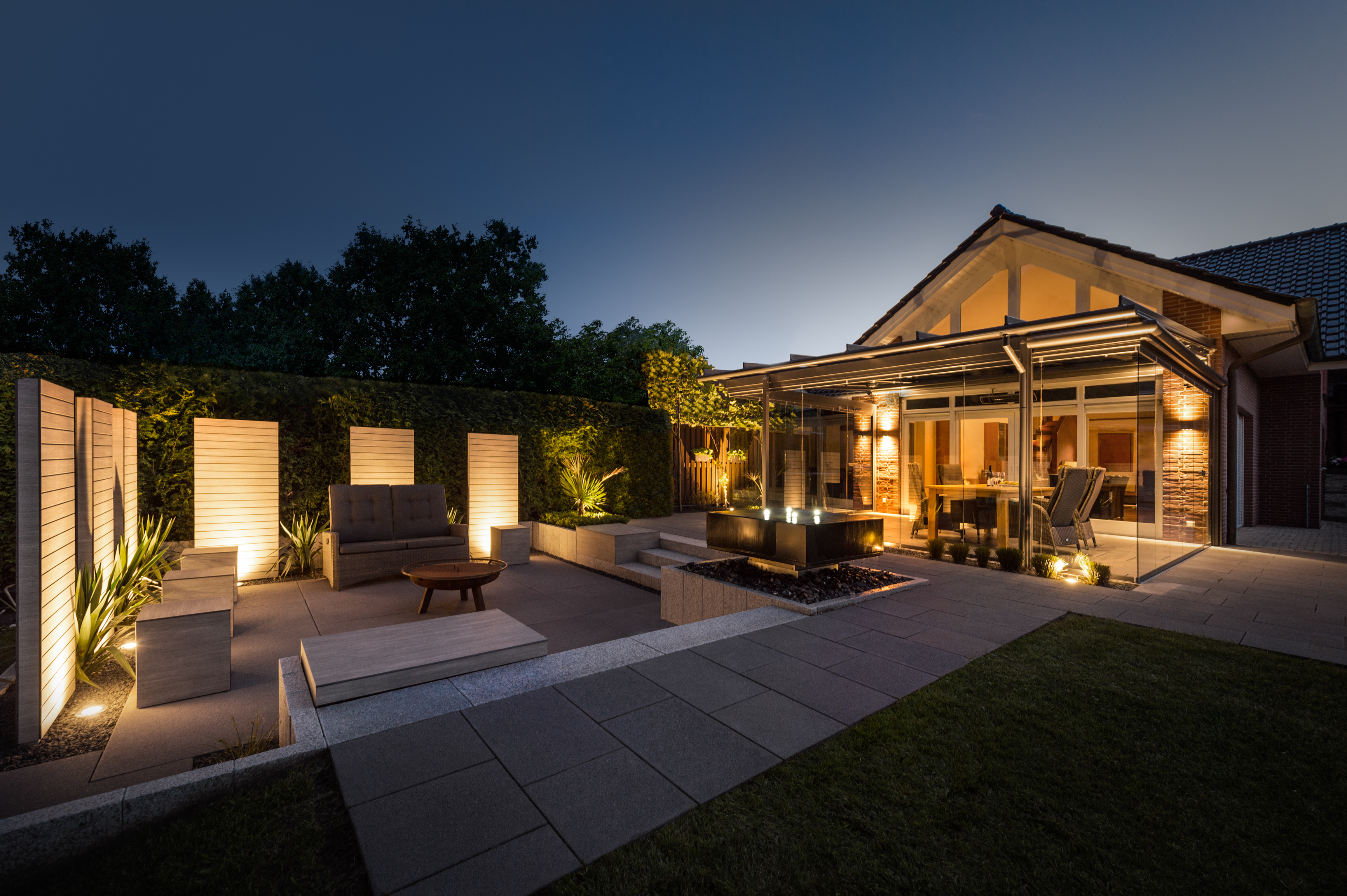 Illuminated patio with garden furniture and glass canopy