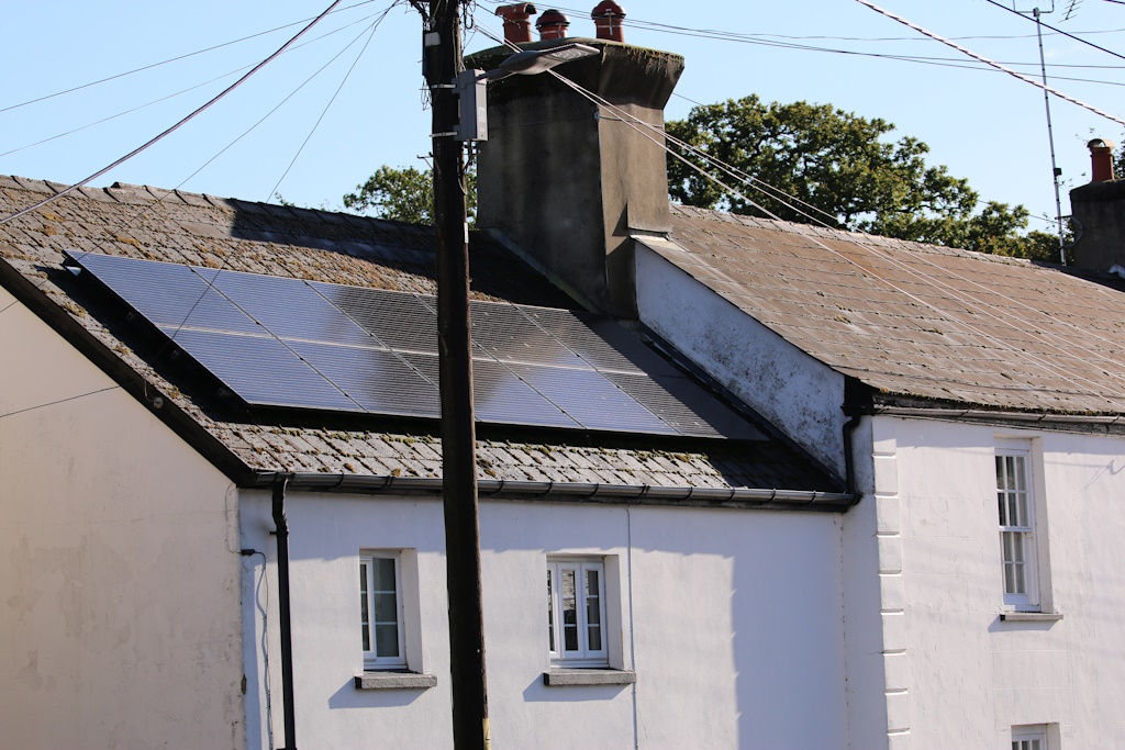 Solar panels installed on the dark roof of a house, against a blue sky