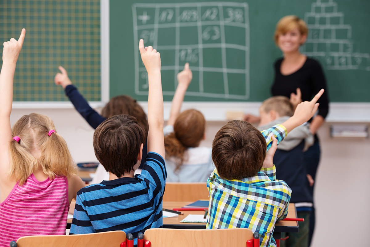  Smiling math teacher in classroom with students waiting with their hands up