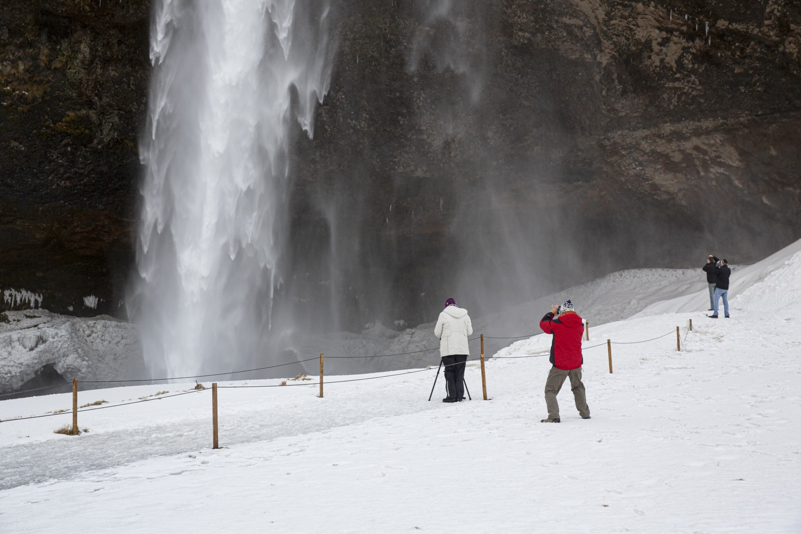 People standing behind a fence in front of Seljalandsfoss waterfall on snowy ground