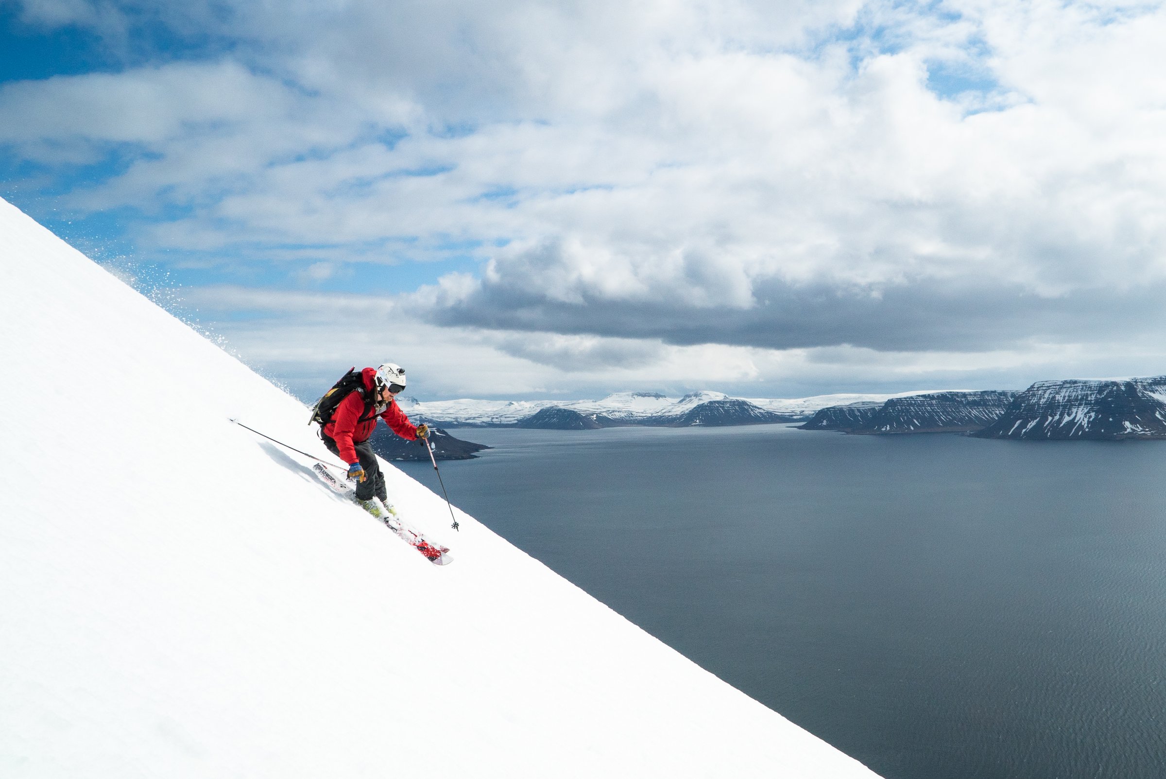 A man skiing down a step mountain, towards the fjord.