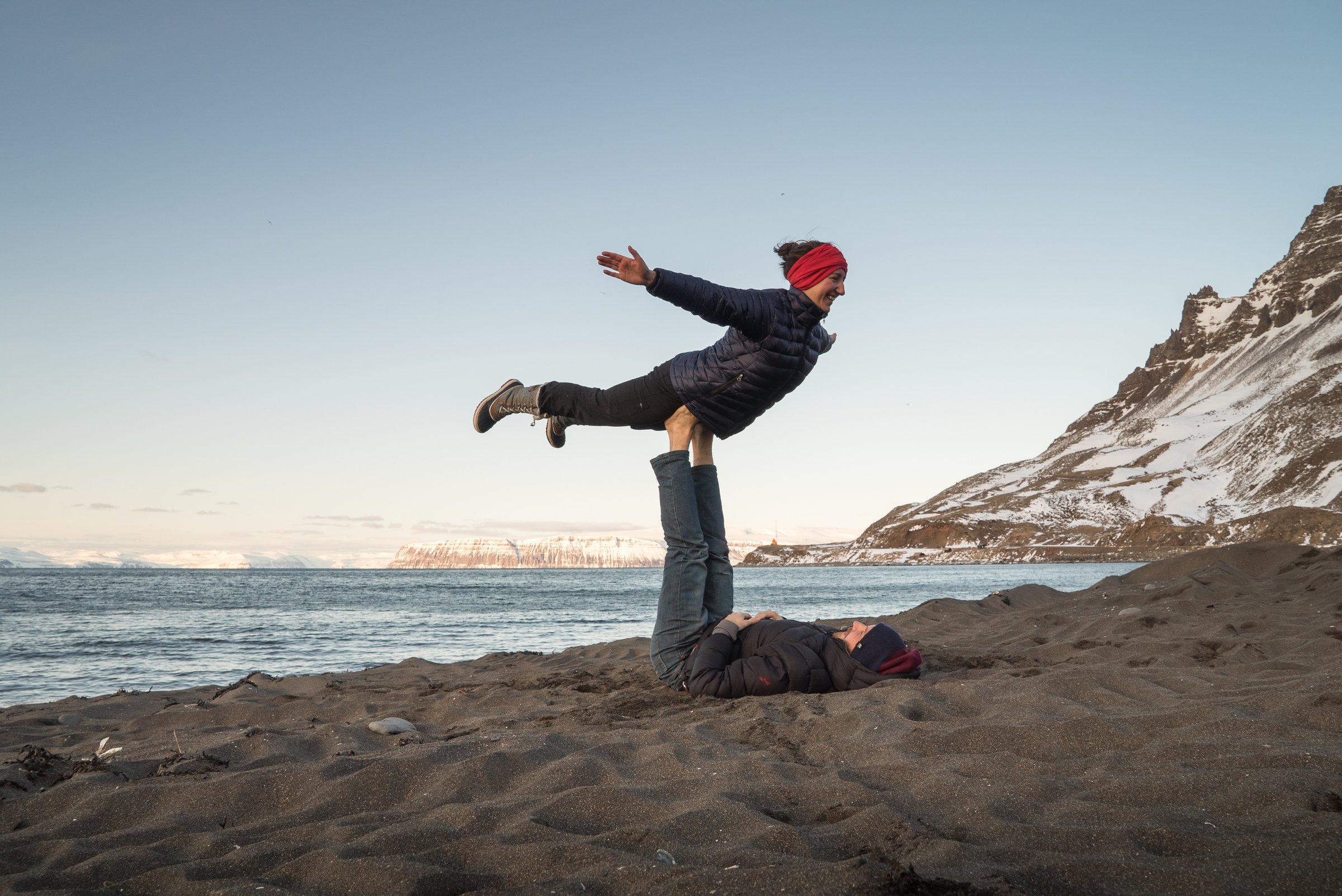 A couple does Yoga on a black sand beach near Bolugnarvík