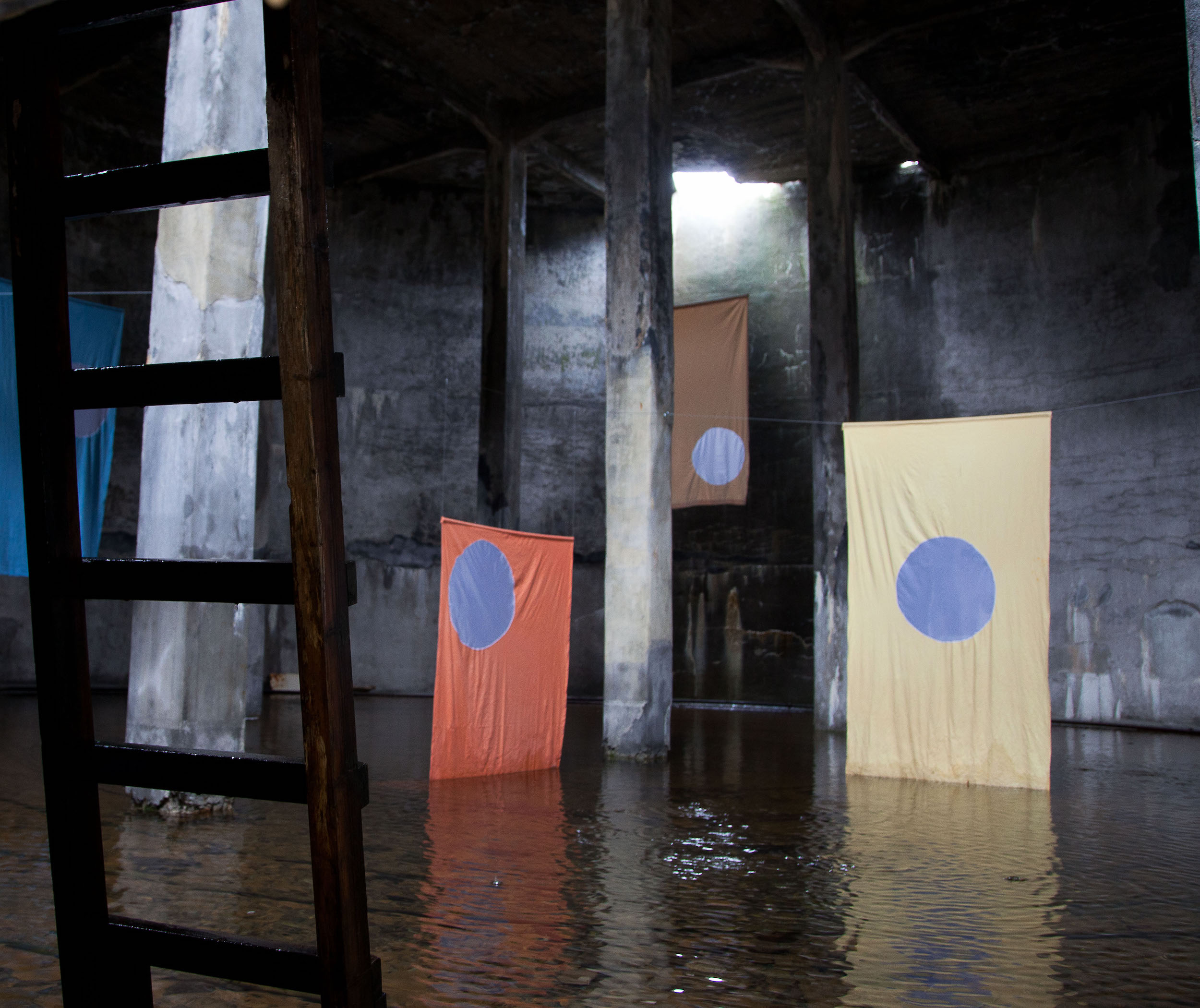 The art piece Hvít sól_White sun shown in the Art exhibition "The Factory" in Djúpavik. An orange, a yellow and a brown cloth hand down the walls of a water tank.