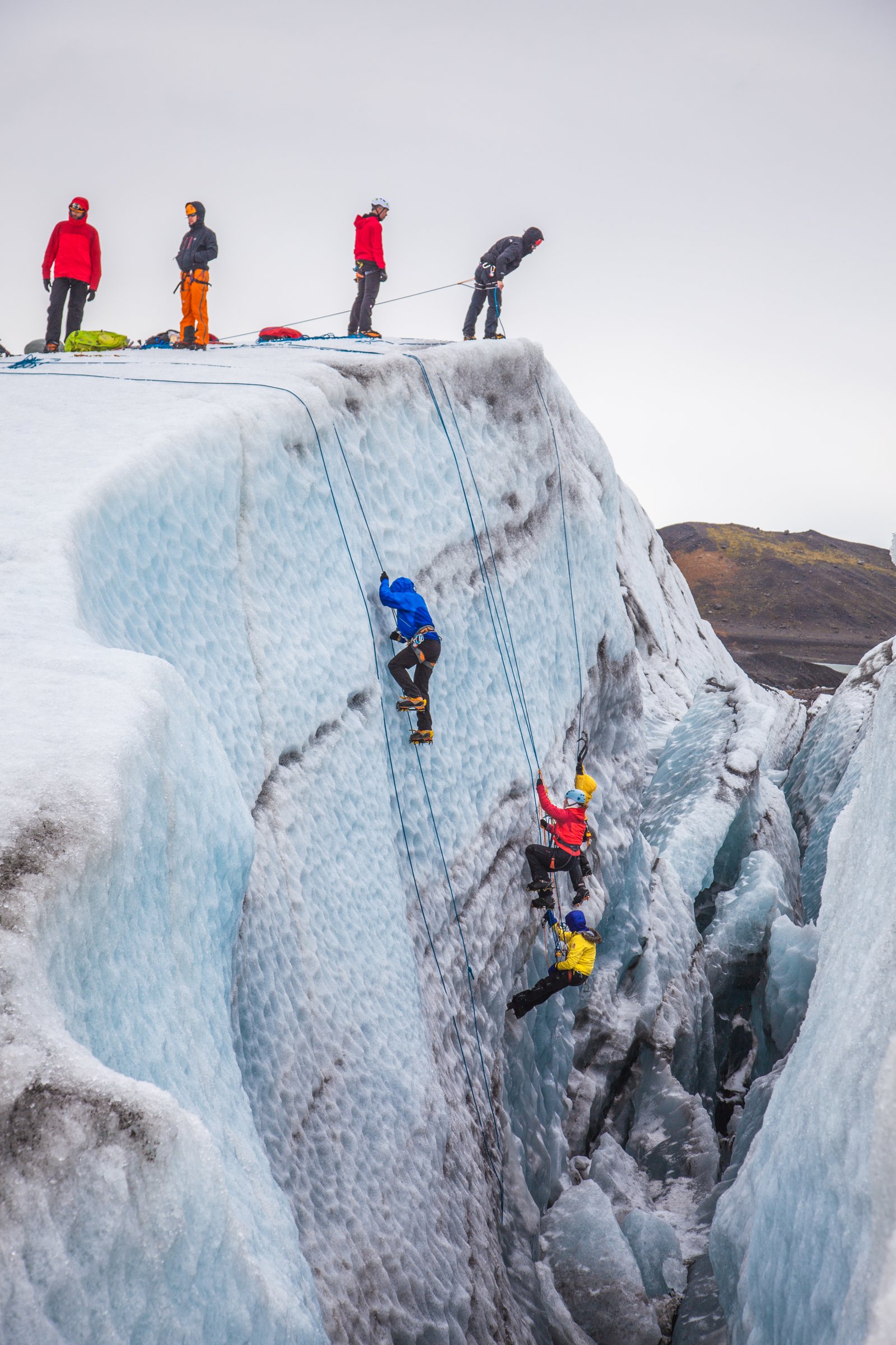 A croup of ice climbers climbing down a glacier wall. Some are waiting on the rim,while others are climbing down.