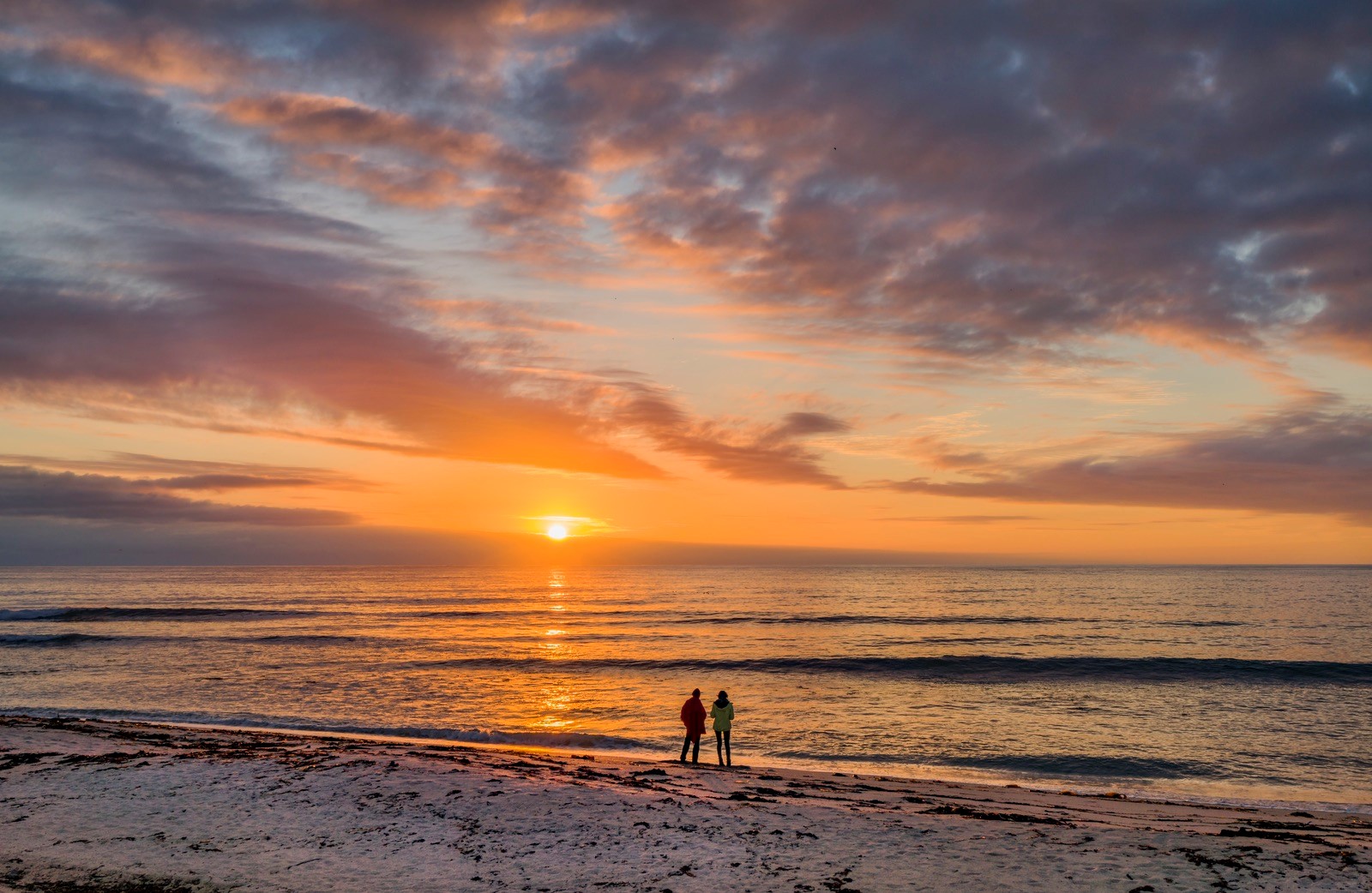A couple at a snowy beach looking at the sunset