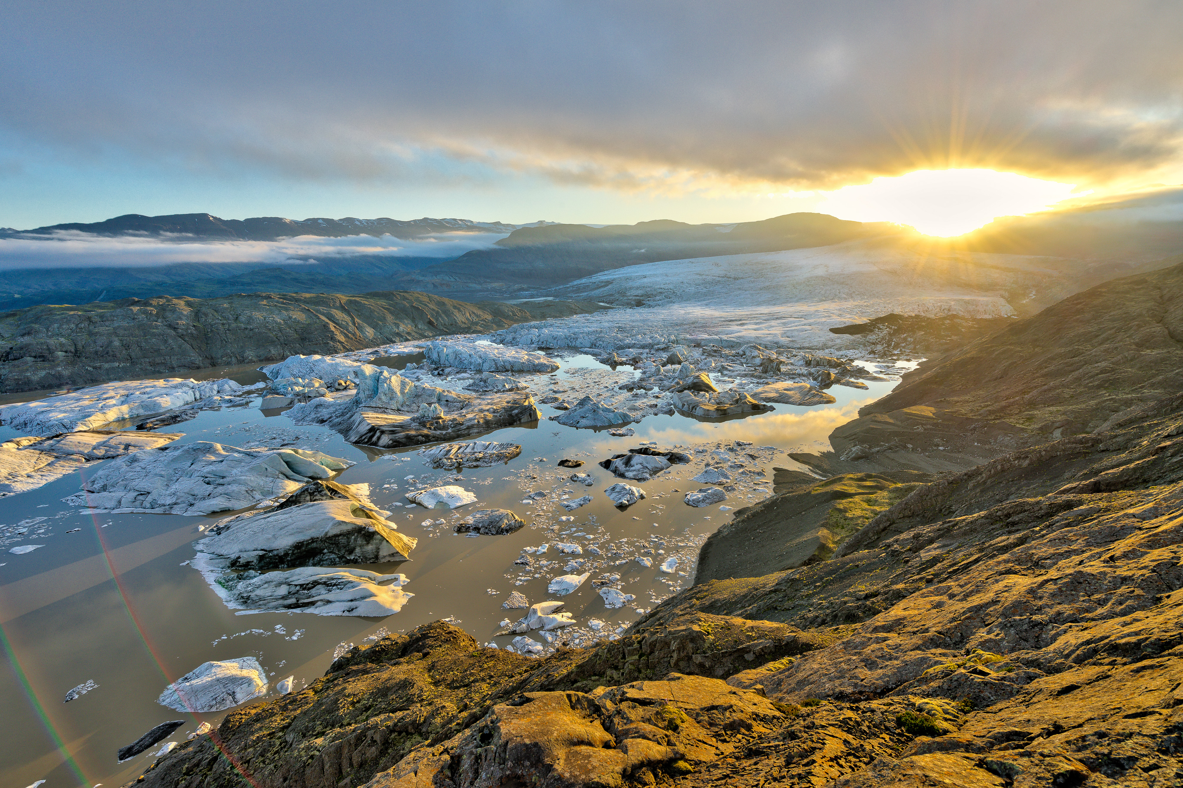 A glacier lake with floating icebergs in front of a river of ice in a sunset atmosphere