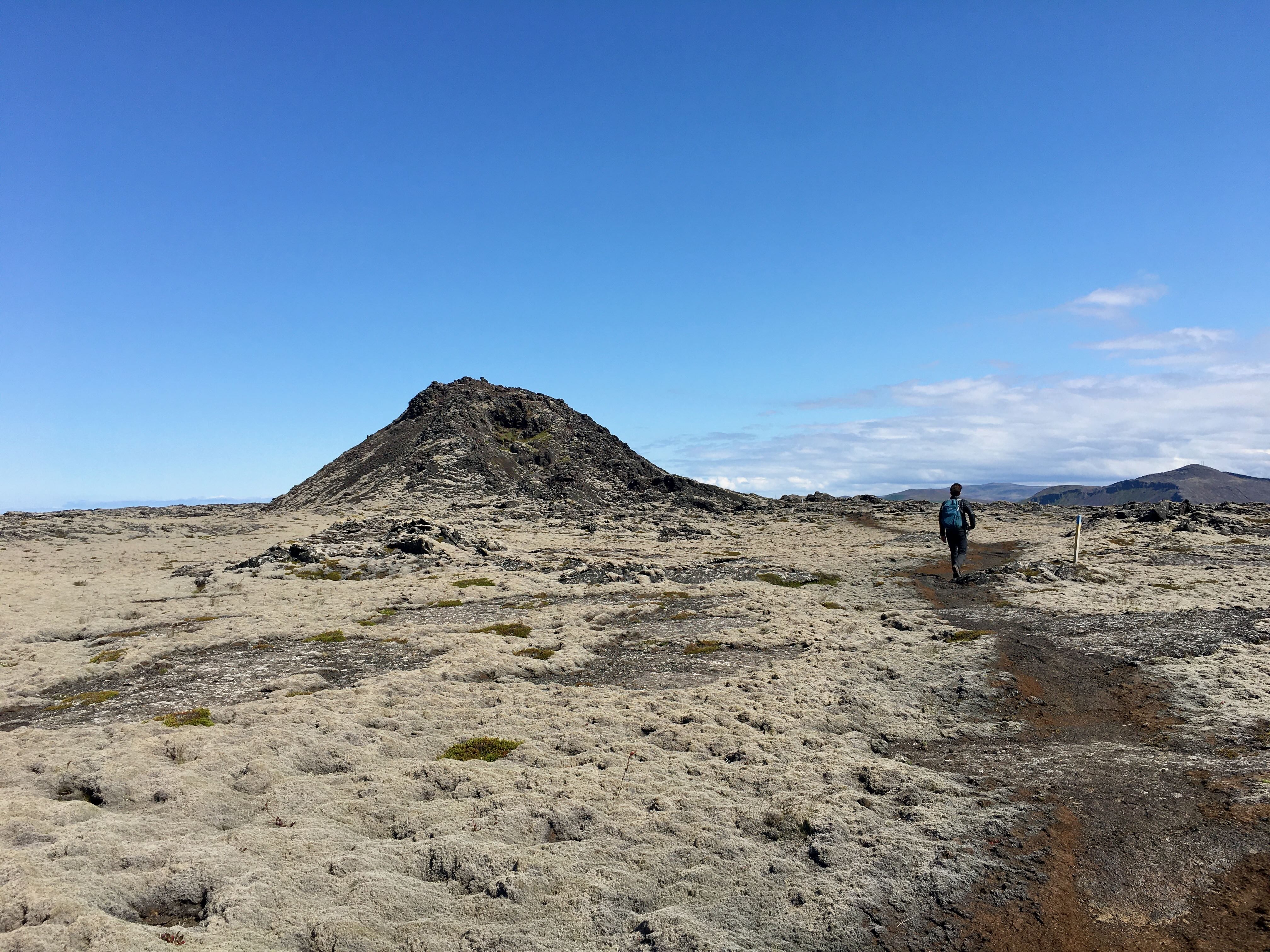 A man hiking between volcanic craters in a moss grown lava field