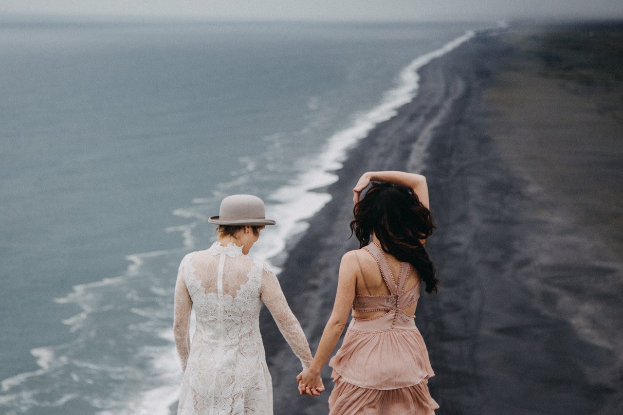 Bride and Bride holding hands above black sand beach