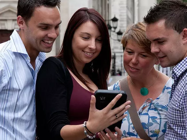 People looking interested while a lady shows them what is on her smart phone