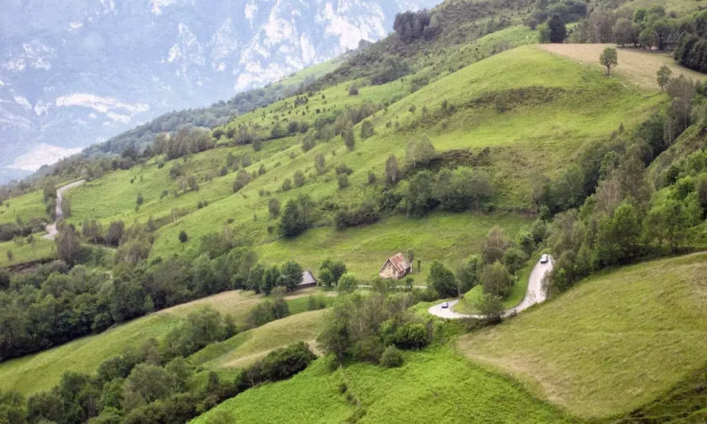 Hilly terrain with fields, trees, small houses and mountains in the background