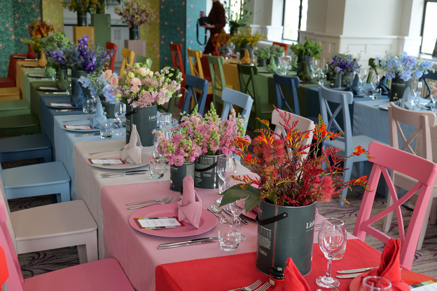 Long tables with Little Greene paint tins holding flowers, along with multi-colored tablecloths, chairs and plates.