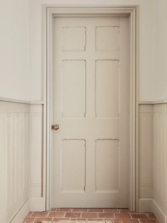 A hallway painted in the light neutral 'Portland Stone - Light' on the upper walls with panelling on the lower walls, door and trim in the darker tonal neutral, Portland Stone.